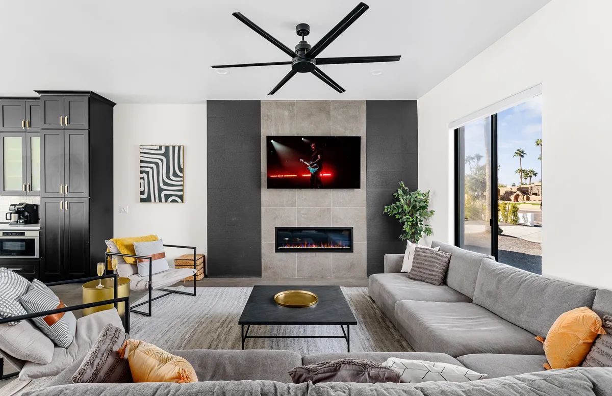 A spacious, modern living room featuring a large, comfortable sectional sofa, a sleek modern fireplace, a large flat-screen TV mounted on the wall, and a stylish coffee table. The room is designed for both relaxation and entertaining, with plenty of seating for gatherings and a cozy atmosphere ideal for movie nights or cheering on a favorite team.