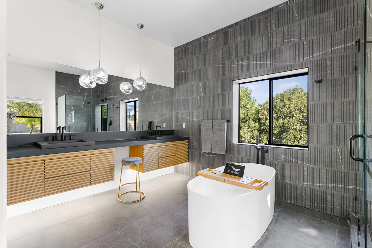 A luxurious spa-style bathroom boasting a freestanding soaking tub, an expansive double-sink vanity, and a large window offering tranquil natural views. The space feels airy, calm, and rejuvenating, perfect for unwinding after a long day.