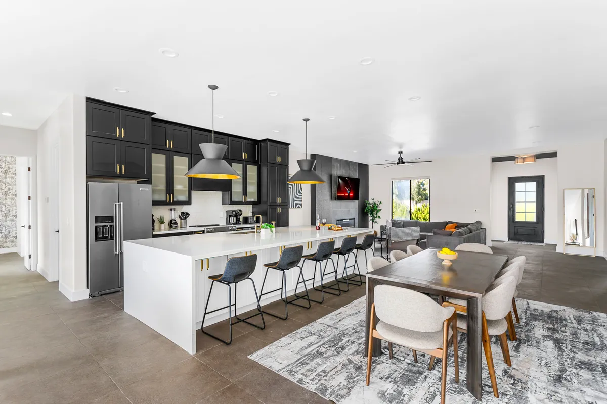 An inviting kitchen and dining space with a large kitchen island, a modern dining table, contemporary appliances, and expansive windows that flood the area with natural light. The open-plan design connects the kitchen and dining area, fostering easy interaction among guests.