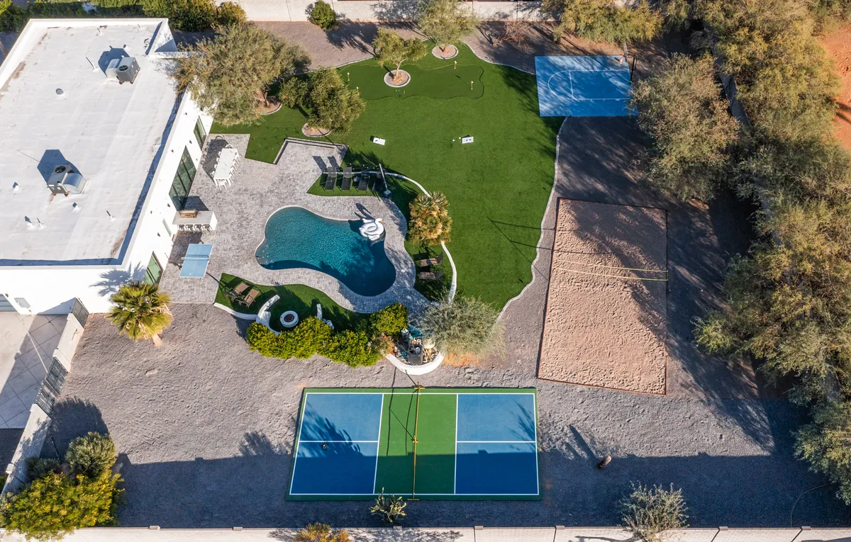 The image captures the home's vibrant backyard at sunset, showcasing a sparkling swimming pool surrounded by lush landscaping, a private tennis court, inviting outdoor seating, and ample space for group gatherings. The scene exudes a lively, resort-style atmosphere with plenty of room for both relaxation and play.