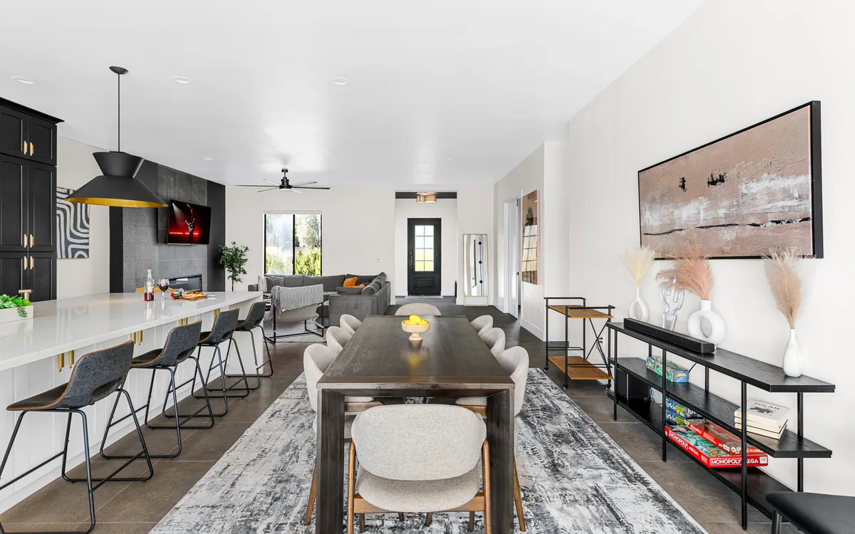 A contemporary open-plan dining and living area, featuring a long table for group meals, a cozy sofa, large window, and vibrant wall art. The setup is ideal for family dinners, game nights, or shared relaxation after a day of exploring.