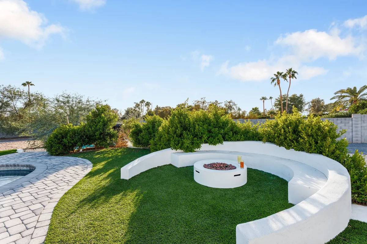 A cozy, curved outdoor seating area wrapped around a glowing fire pit, surrounded by lush greenery. This space invites guests to unwind, enjoy drinks, and share laughter in a relaxed, intimate setting.