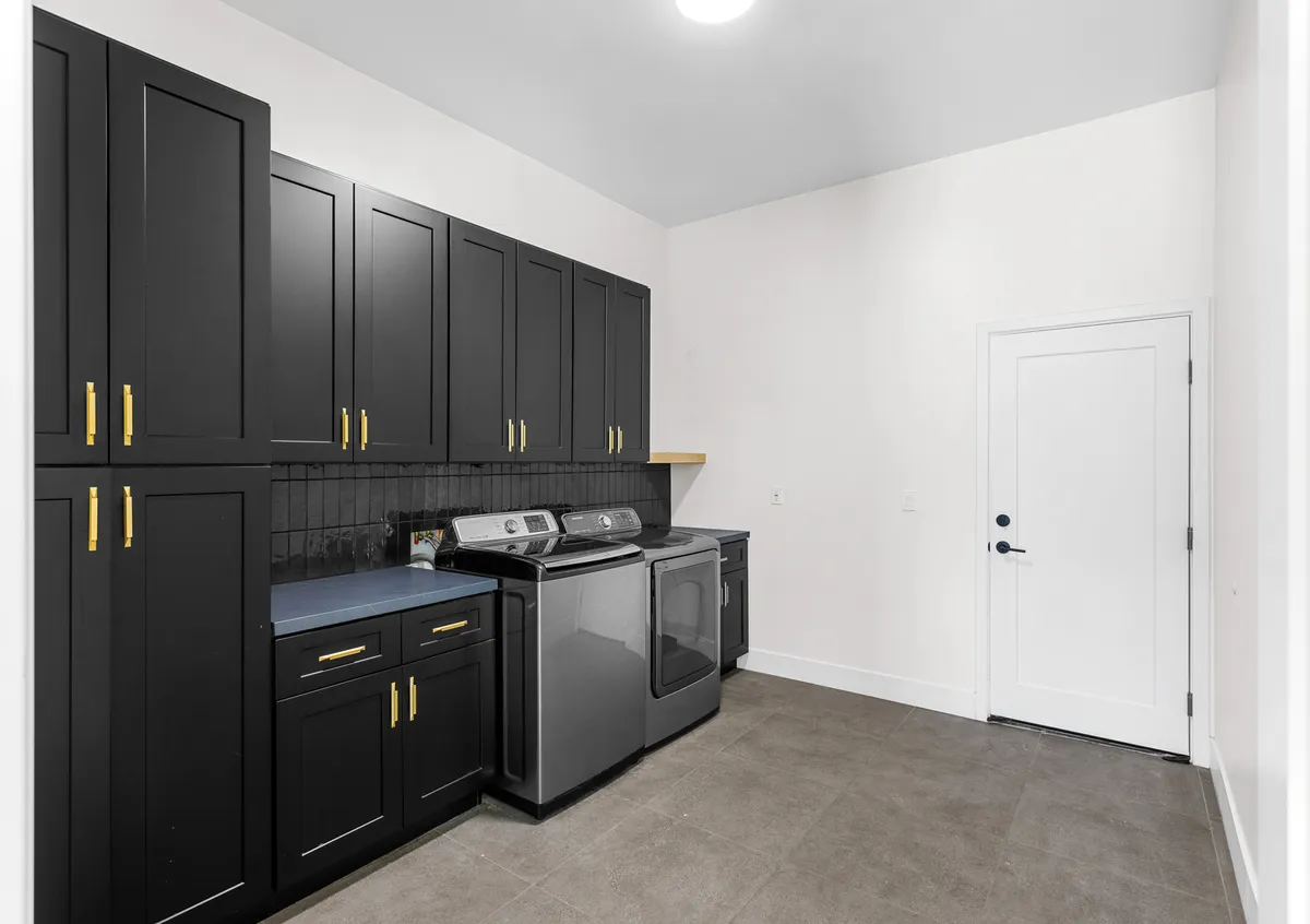 A modern laundry and storage room with black cabinetry, silver appliances, and organized shelving. The efficient design provides ample storage for family gear, extra bedding, or baby equipment.