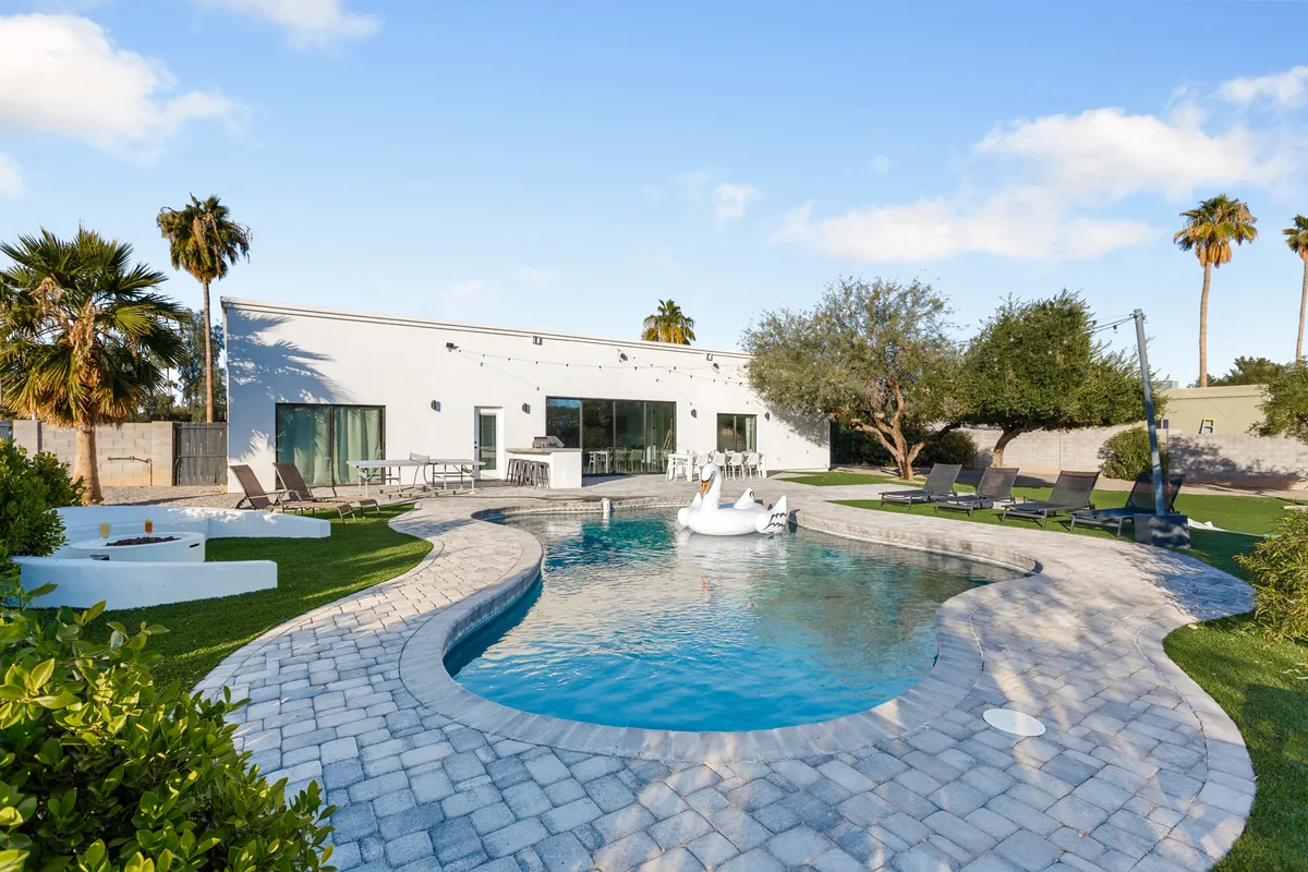 This inviting exterior shot captures a modern home's swimming pool surrounded by lounge chairs, palm trees, and a stylish facade, all bathed in sunset light. The scene radiates relaxation and fun, suggesting a backyard oasis where families can gather and play together.