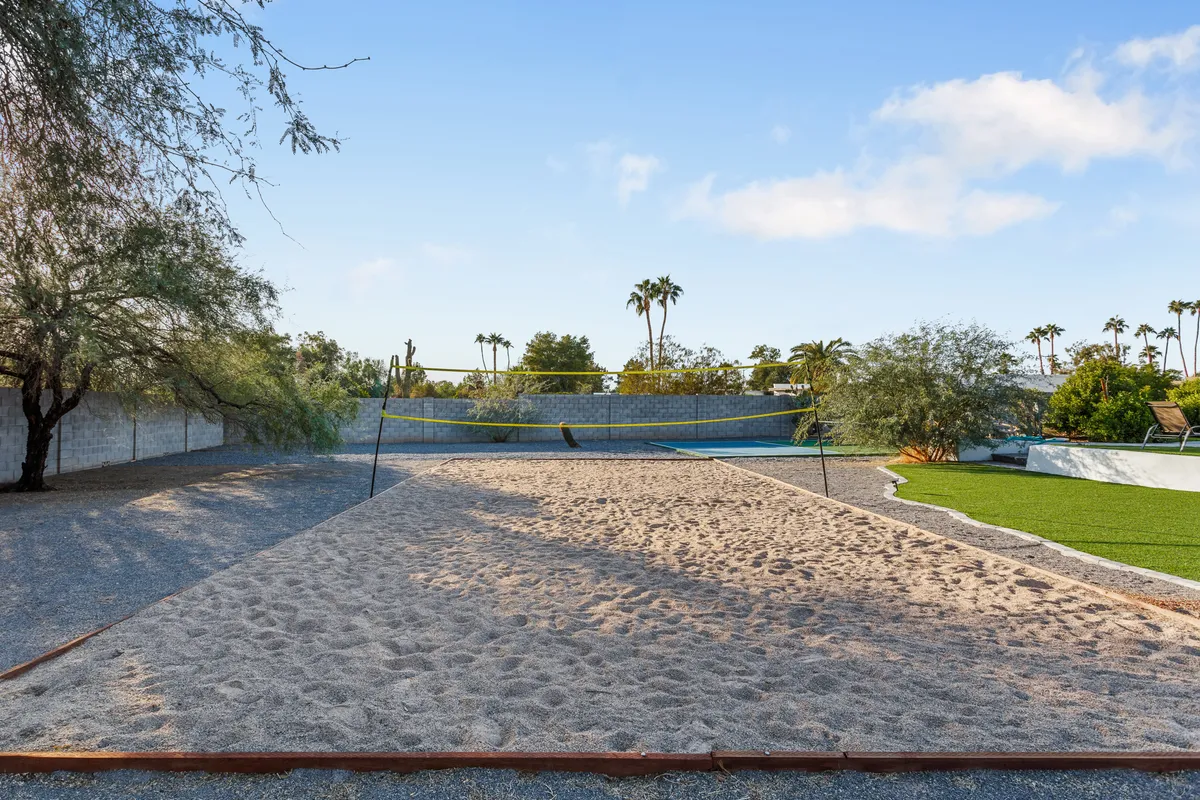 A lively sand volleyball court surrounded by palm trees and greenery. The sand area is inviting, with plenty of space for team games and social gatherings, evoking an energetic and playful vibe.