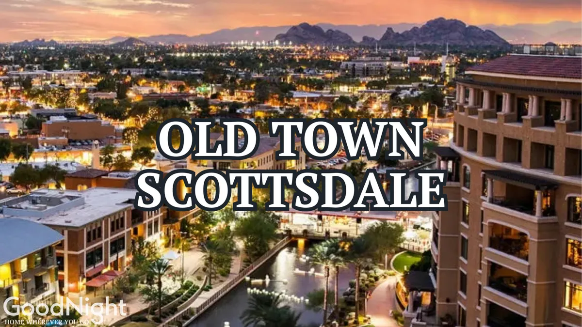 An iconic view of Old Town Scottsdale at dusk, featuring the well-lit 'Old Town Scottsdale' sign, bustling illuminated buildings, a shimmering waterway, and a mountain backdrop. The lively streetscape hints at vibrant nightlife and entertainment options nearby.